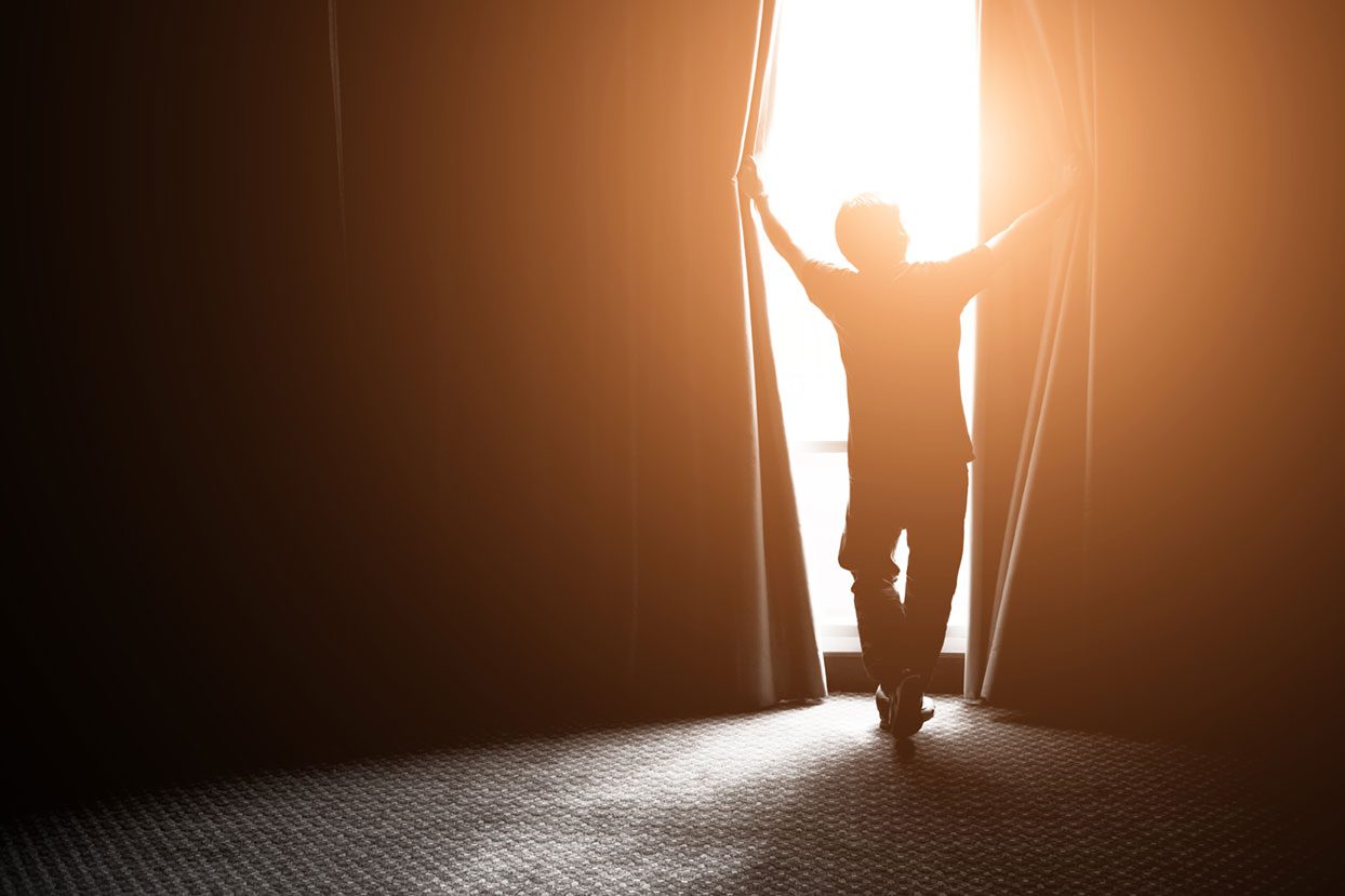 Man opening curtains as sunlight streams in